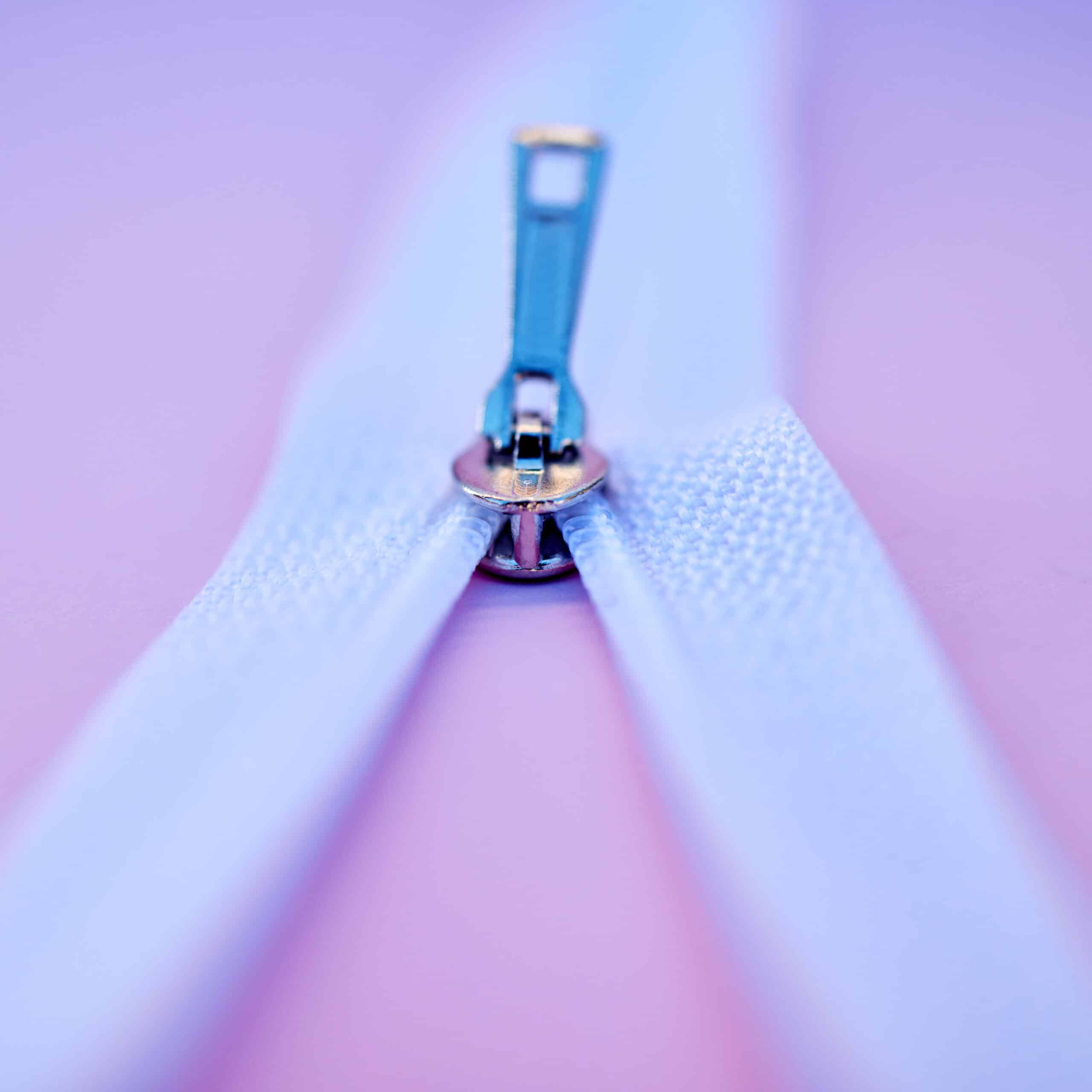 Closeup of a metal zip isolated on a pink background. Macro view of a zipper closing or being unzip