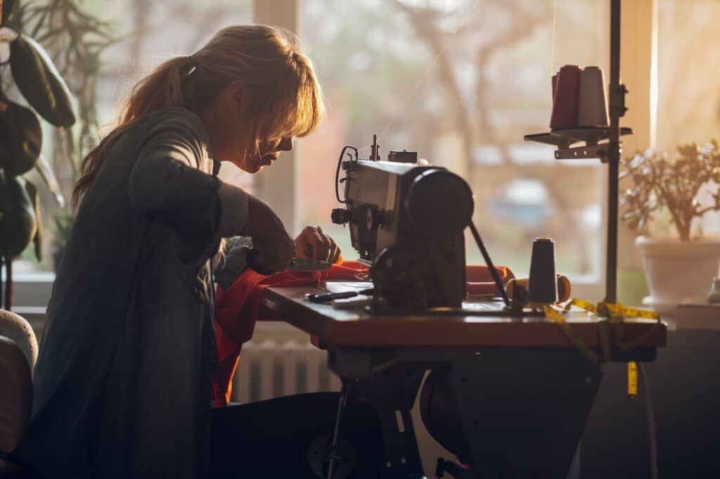 Tailor woman sitting and sewing on a sewing machine a in studio